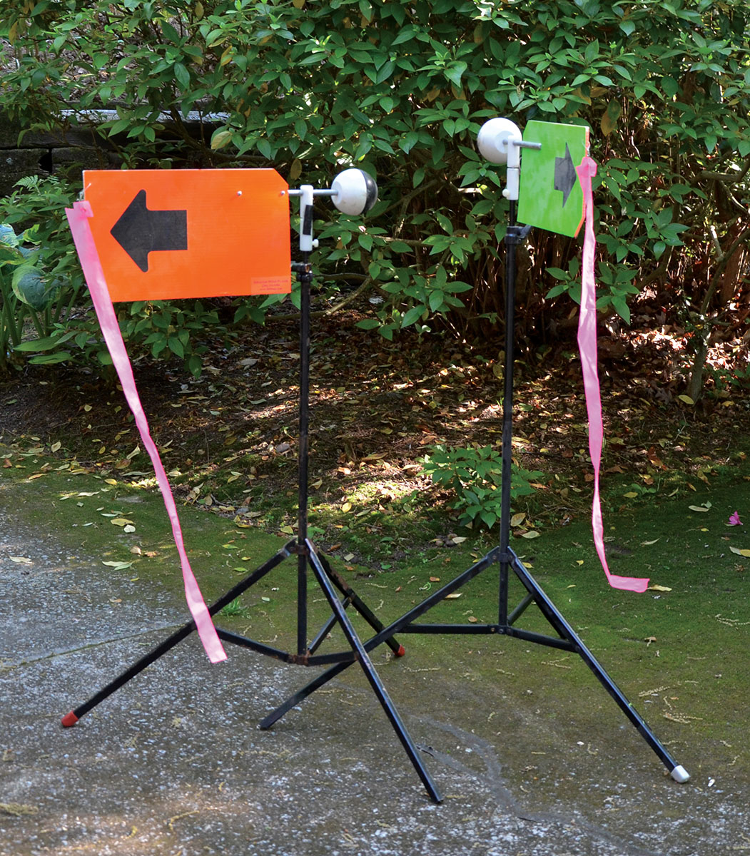 Graham wind flags, one placed 15 yards downrange and the other adjacent to the target, are positioned so they can be observed in the scope while its crosshairs are on the aiming point of the target. In addition to indicating wind direction and intensity, they also show whether the wind is incoming or outgoing.